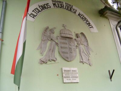 Dugovics emléktábla a Nagysimonyi iskola homlokzatán az angyalos címerrel. (Fotó: 2004. év)